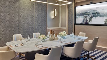 Un salón de conferencias con una mesa de mármol, sillas blancas y vista a la ciudad.
