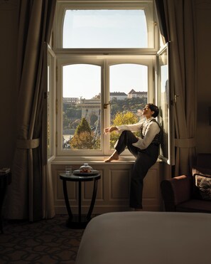 A room with a large window, a bed, a small table with a glass of water, and a chair.