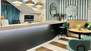 Uma área de recepção moderna com balcão curvo, um computador de mesa e um espaço de estar com duas cadeiras e uma pequena mesa.