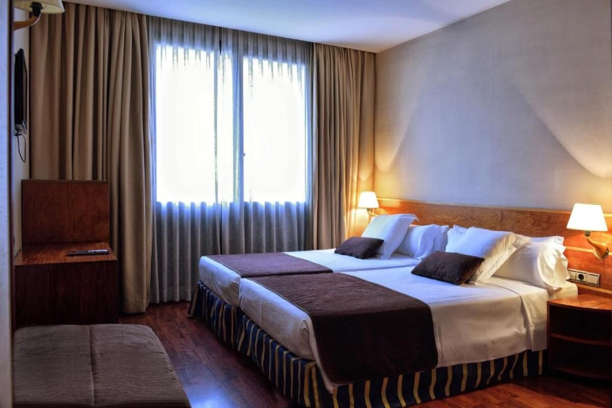 Habitación de hotel con dos camas, televisión, escritorio y ventana con cortinas.