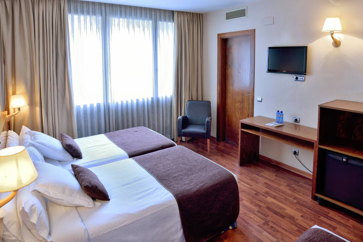 Een hotelkamer met twee bedden, een bureau, een stoel, een televisietoestel en een lamp.