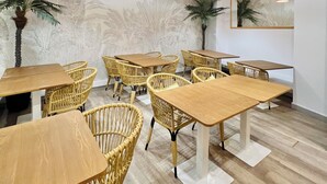Interior de restaurante com mesas de madeira e cadeiras de vime, teto de pedra e iluminação decorativa.