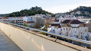 A riverside walkway with a metal railing, overlooking a town with historic buildings and a castle on a hill. - Hotel Pombalense (Pombal)