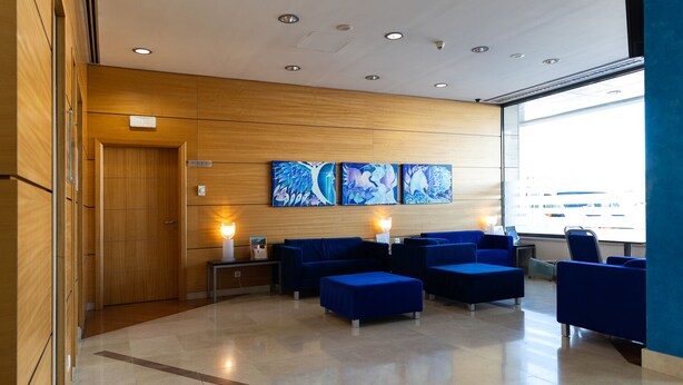 A modern lobby with wooden paneling, a reception desk, blue seating area, and artwork on the wall. - Hotel Pombalense (Pombal)