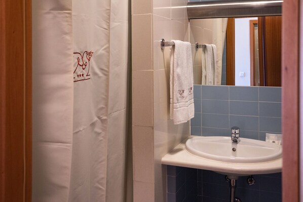 Un baño con lavamanos blanco, azulejos azules y cortina de ducha con un logotipo.