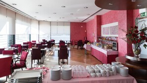 A spacious dining area with tables and chairs, a buffet setup, and a large window providing natural light. - Hotel Pombalense (Pombal)