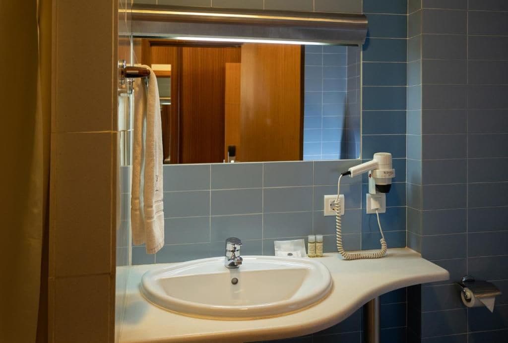 Un bagno con lavandino, specchio, porta asciugamani e asciugacapelli.