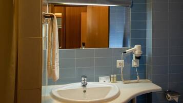 Un bagno con lavandino, specchio, porta asciugamani e asciugacapelli.