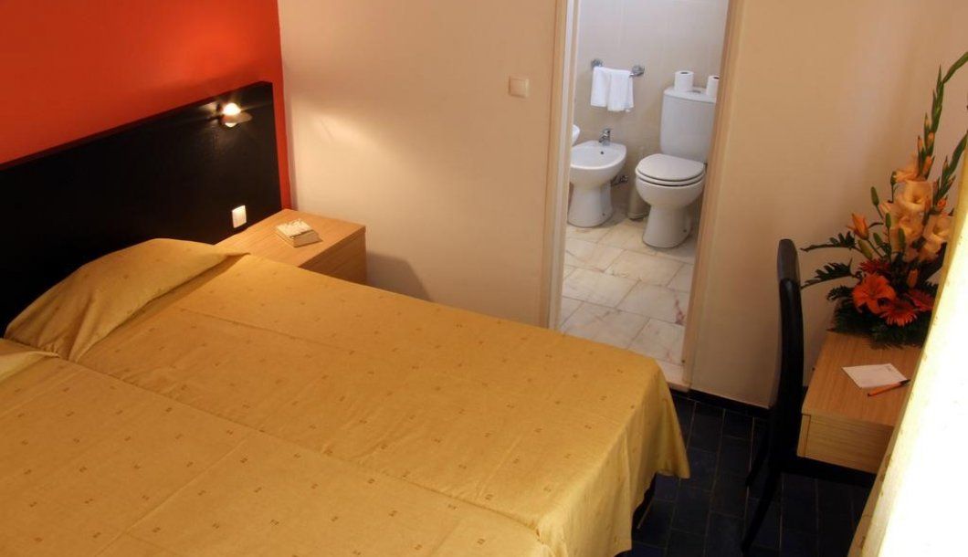 A hotel room with a bed, a nightstand, a small table with a vase of flowers, and a view of the bathroom.