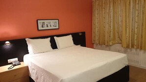 Une chambre d’hôtel avec un lit, une table de chevet avec un téléphone et un tableau accroché au mur.