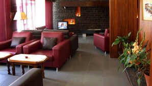 Un hall d’entrée avec des canapés rouges, un téléviseur, une cheminée et une plante en pot.