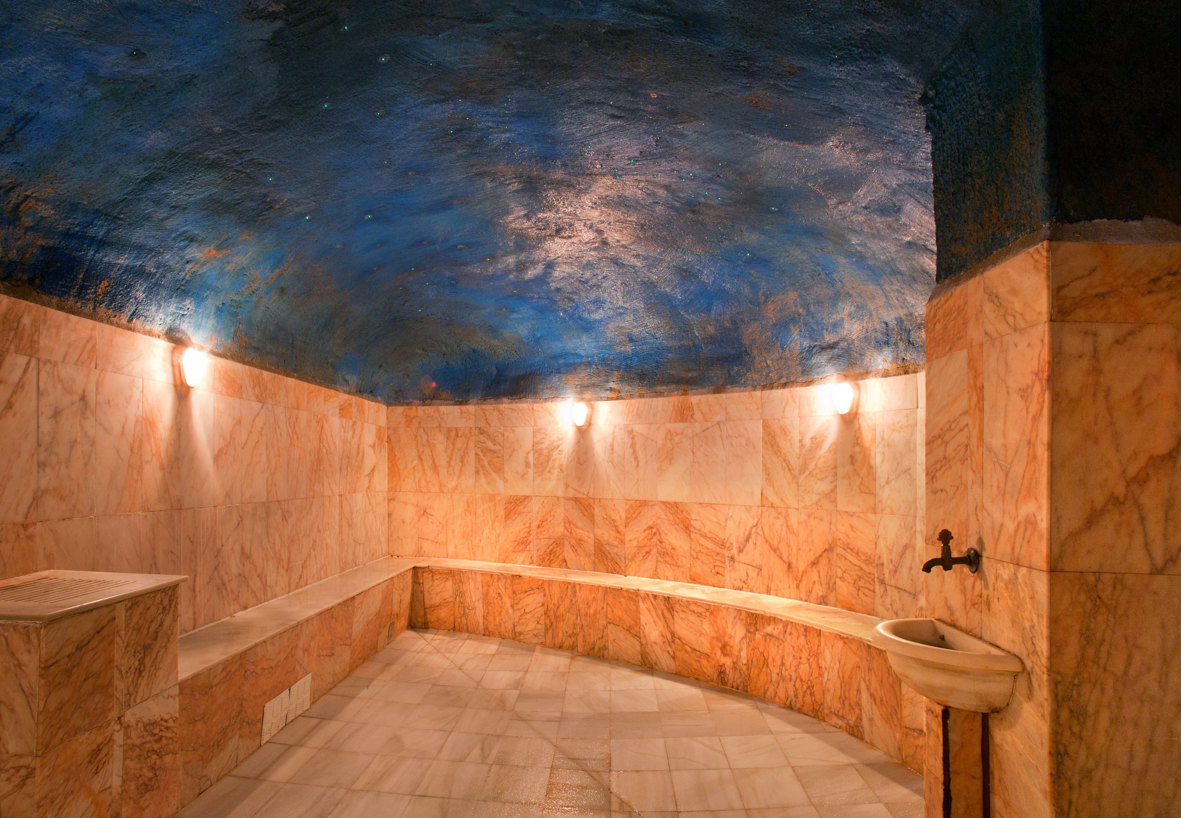 A bathroom with a curved bench, a sink, and a ceiling painted to resemble a starry night sky.