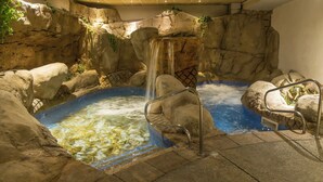 Un área de aguas termales con cascada, paredes de piedra y barandillas de metal.