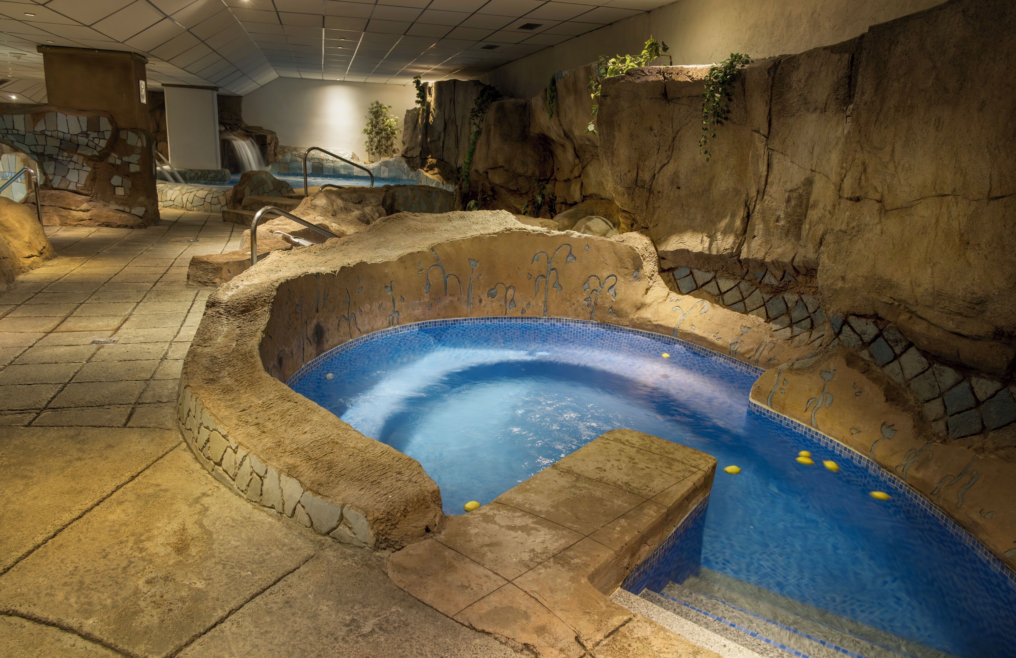 Una piscina interior con diseño de roca natural, una cascada y un sendero de piedra que conduce a la piscina.