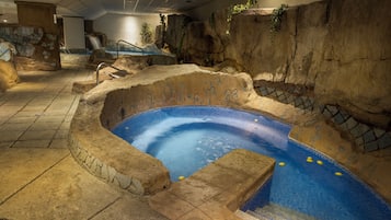Una piscina interior con diseño de roca natural, una cascada y un sendero de piedra que conduce a la piscina.