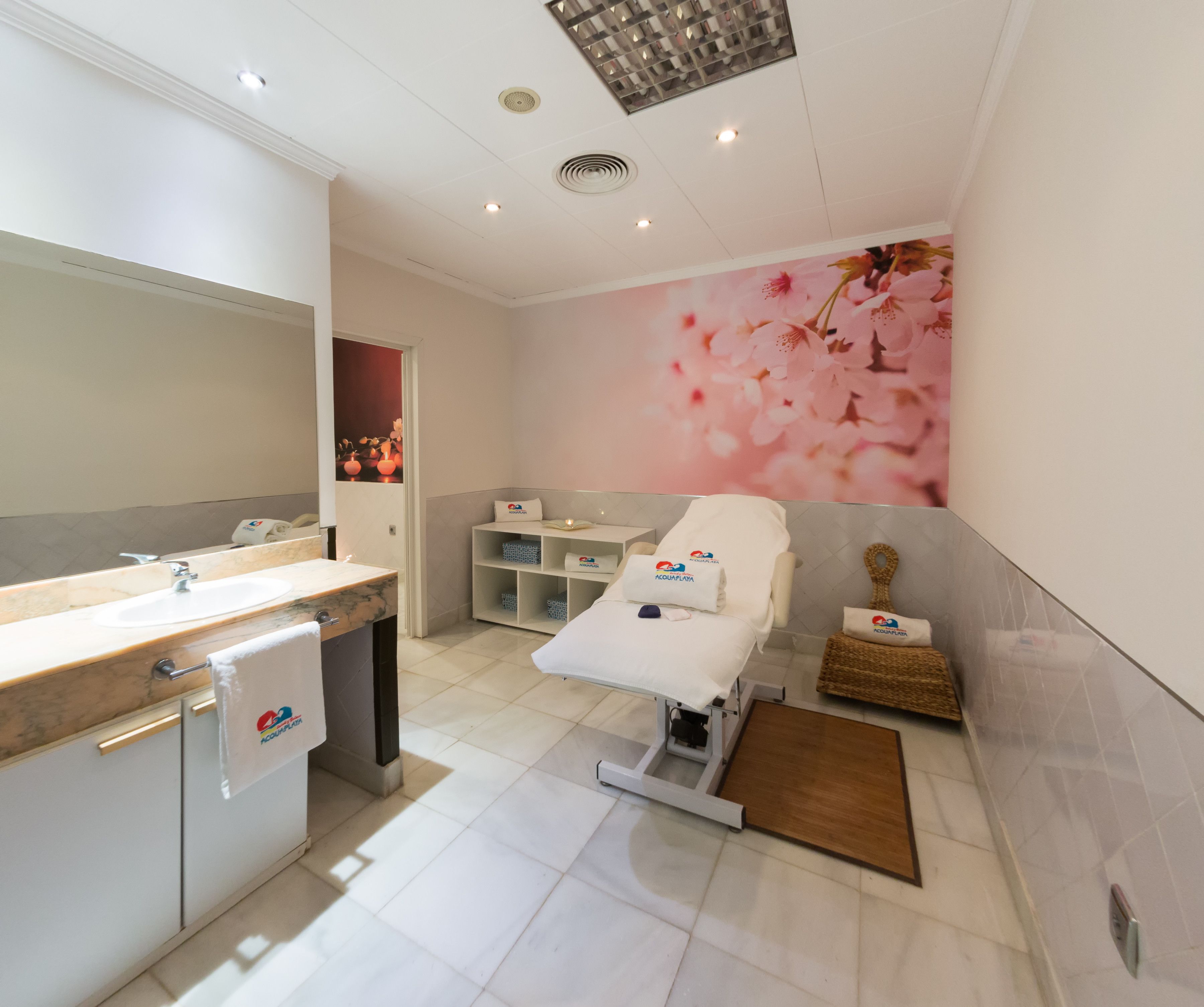 A modern bathroom with a large mirror, a sink, a massage table, and a shelf with towels and toiletries.