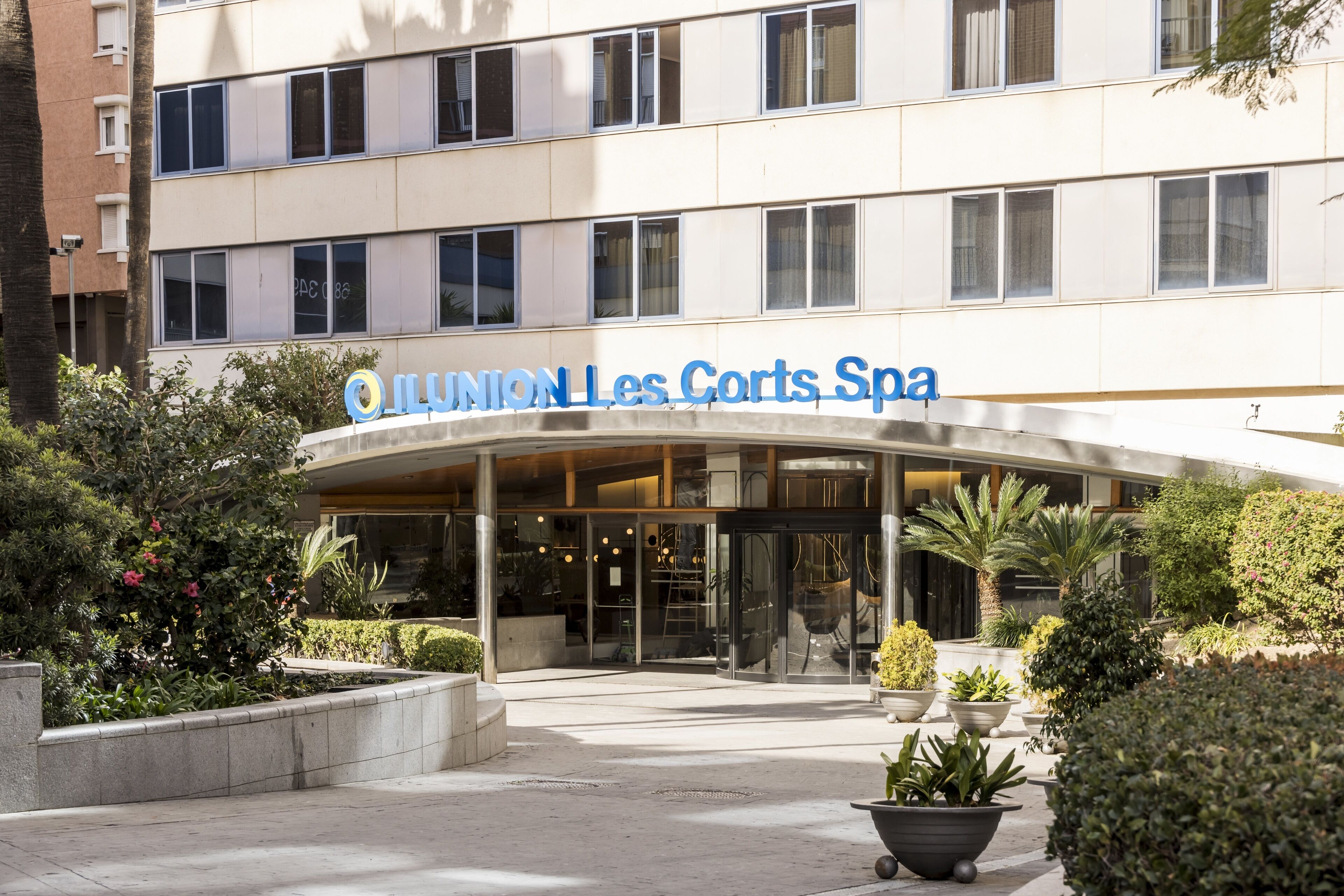 A hotel entrance with a modern design, featuring a curved glass facade and a sign that reads "Union Les Corts Spa".