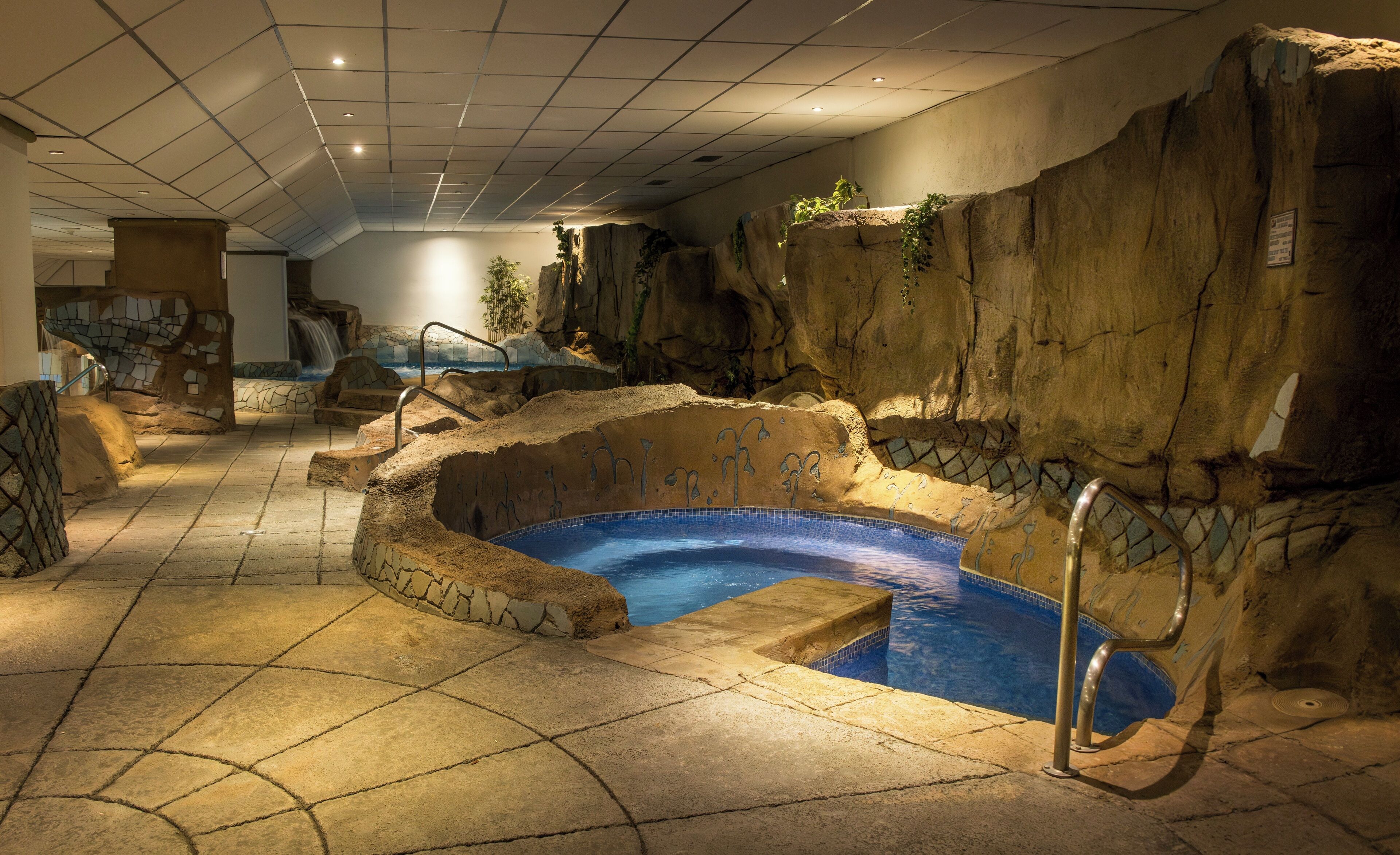 An indoor swimming pool with a rocky design, surrounded by stone walls and a tiled floor.