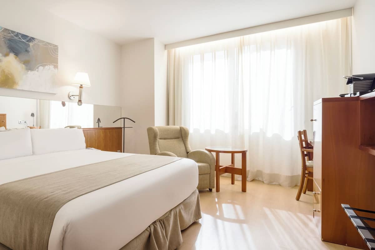 A hotel room with a large bed, a desk, a chair, a television, and a painting on the wall.