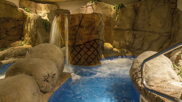Un área de aguas termales con una cascada, rodeada de formaciones rocosas y una piscina con azulejos.