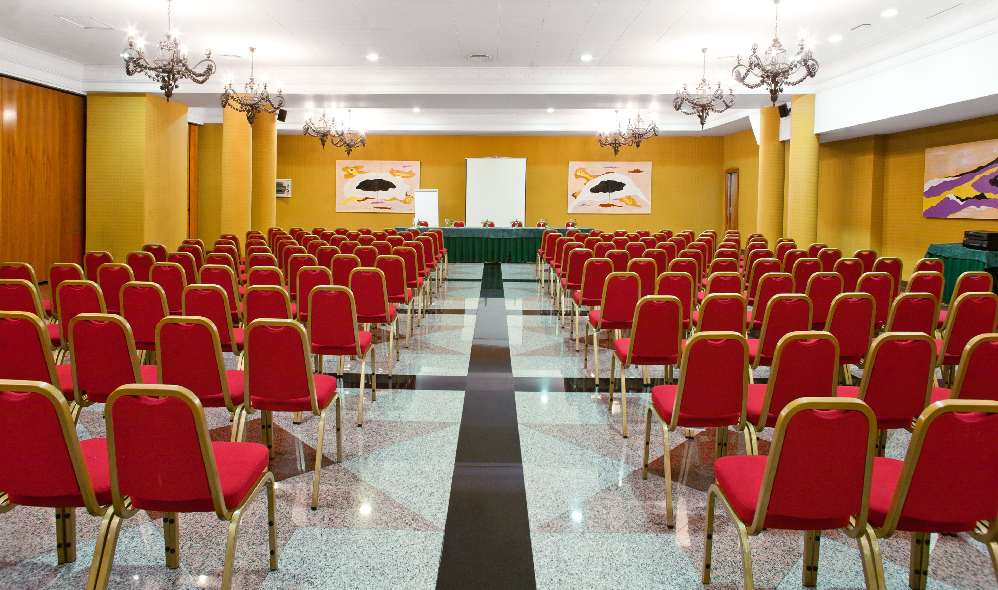 A conference room with rows of red chairs, a long table, and chandeliers.