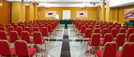 A conference room with rows of red chairs, a long table, and chandeliers.