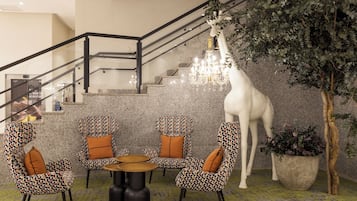 Un vestíbulo con sillones estampados, un candelabro, una escalera y una planta grande en maceta.