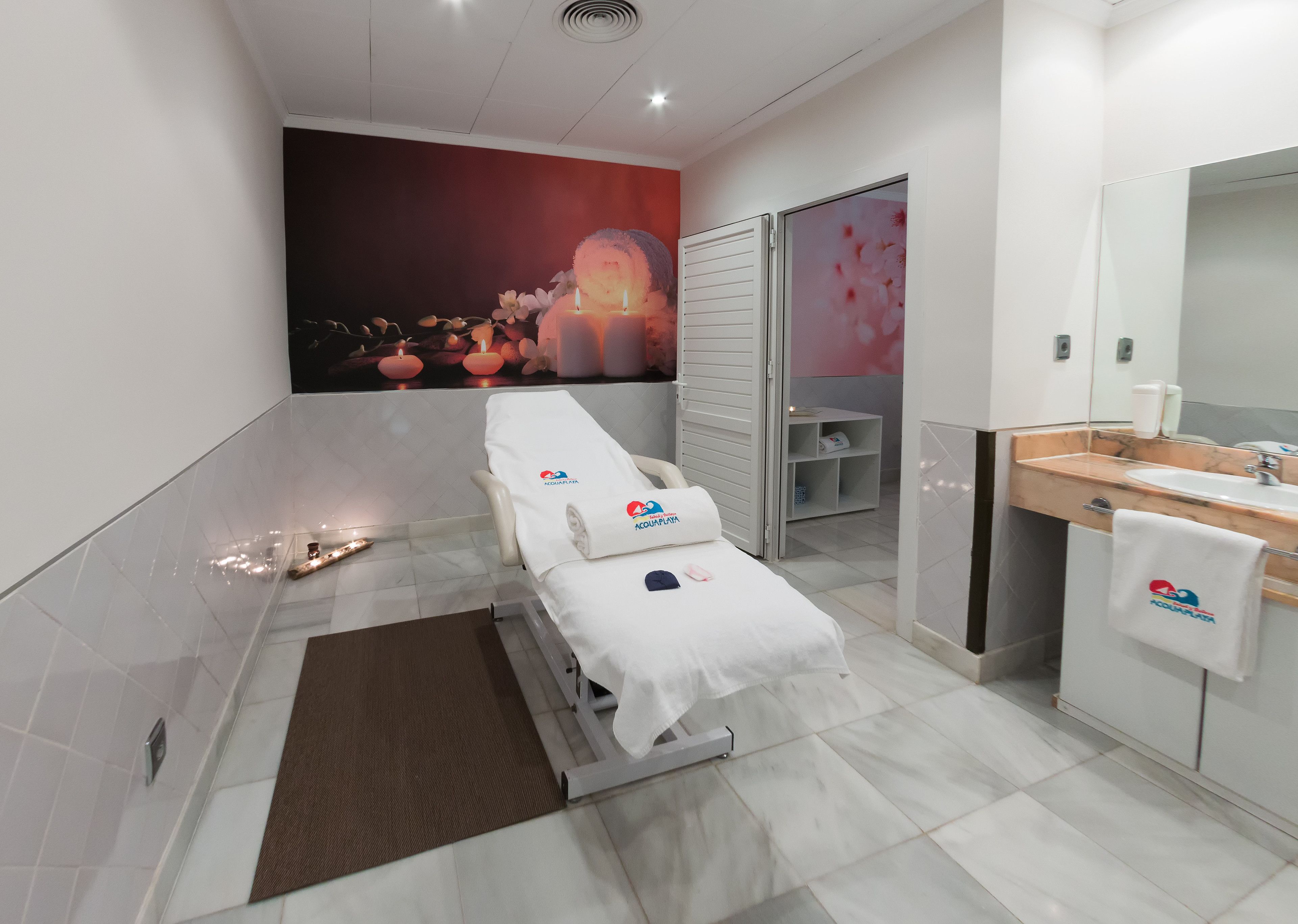 Une salle de spa moderne équipée d’une table de soins, d’un grand miroir et d’un espace lavabo.