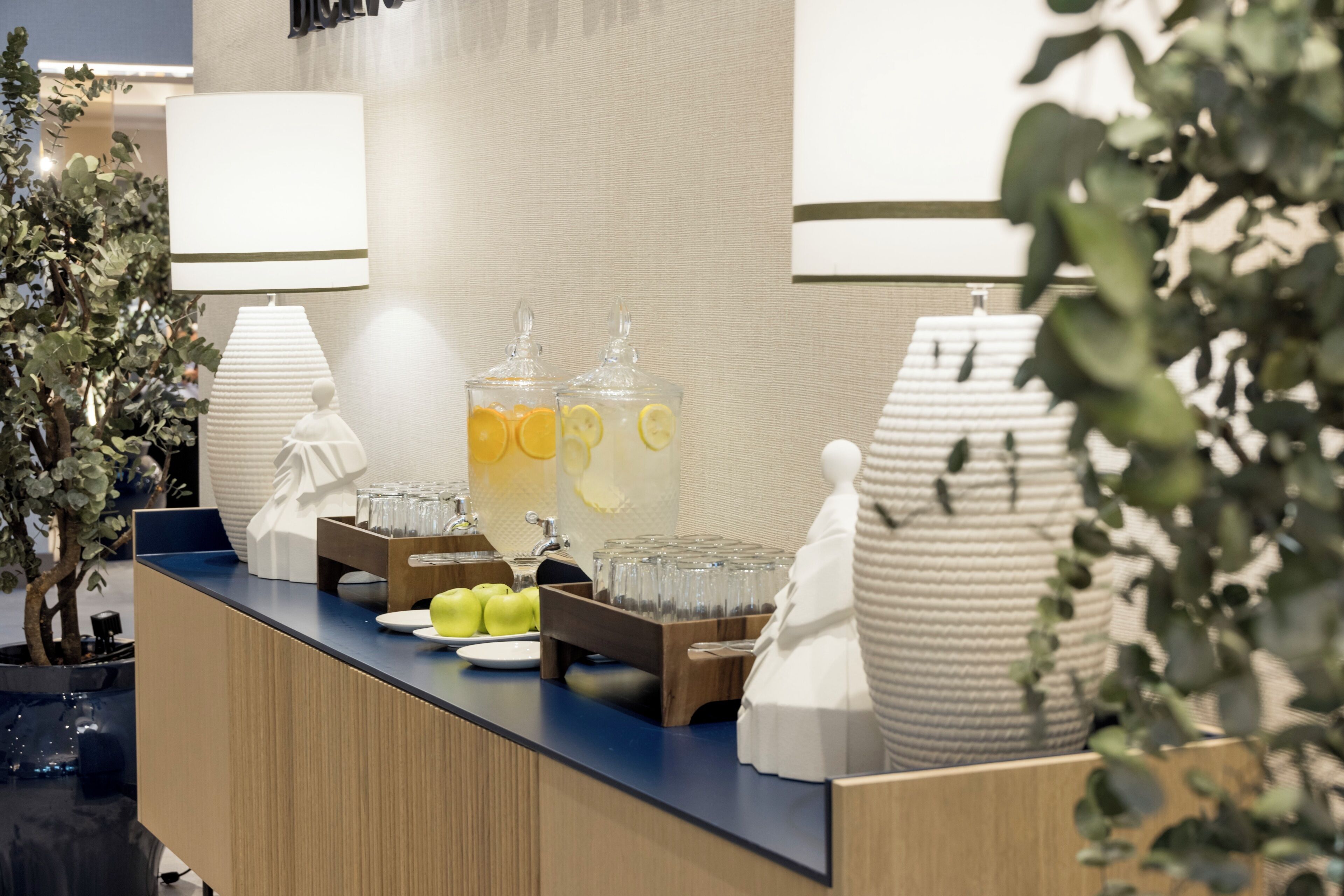 A hotel reception area with a counter, glass containers with beverages, a lamp, and decorative vases.