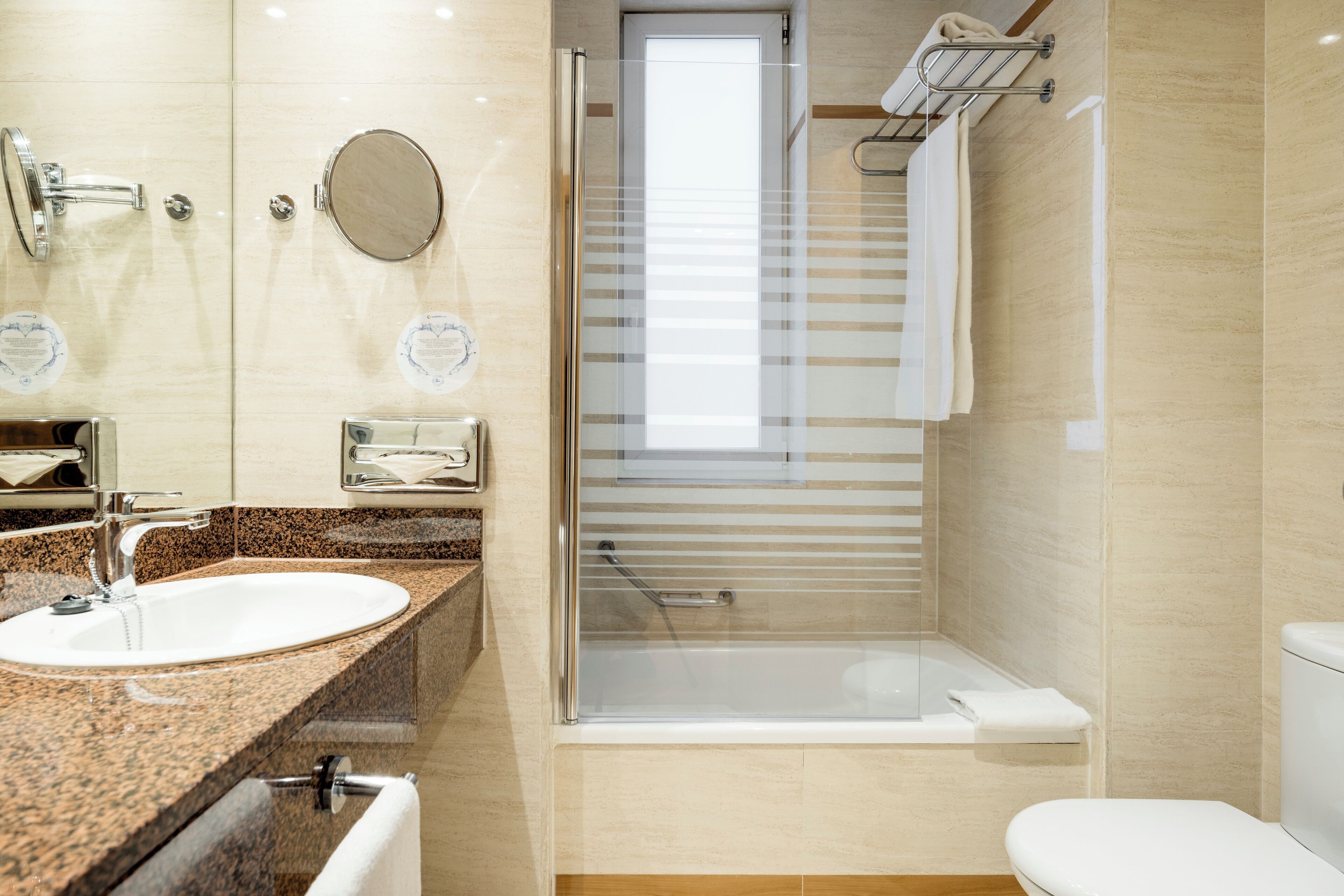 A modern bathroom with a granite countertop sink, a glass-enclosed shower, and a white toilet.