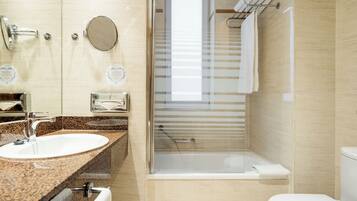 A modern bathroom with a granite countertop sink, a glass-enclosed shower, and a white toilet.