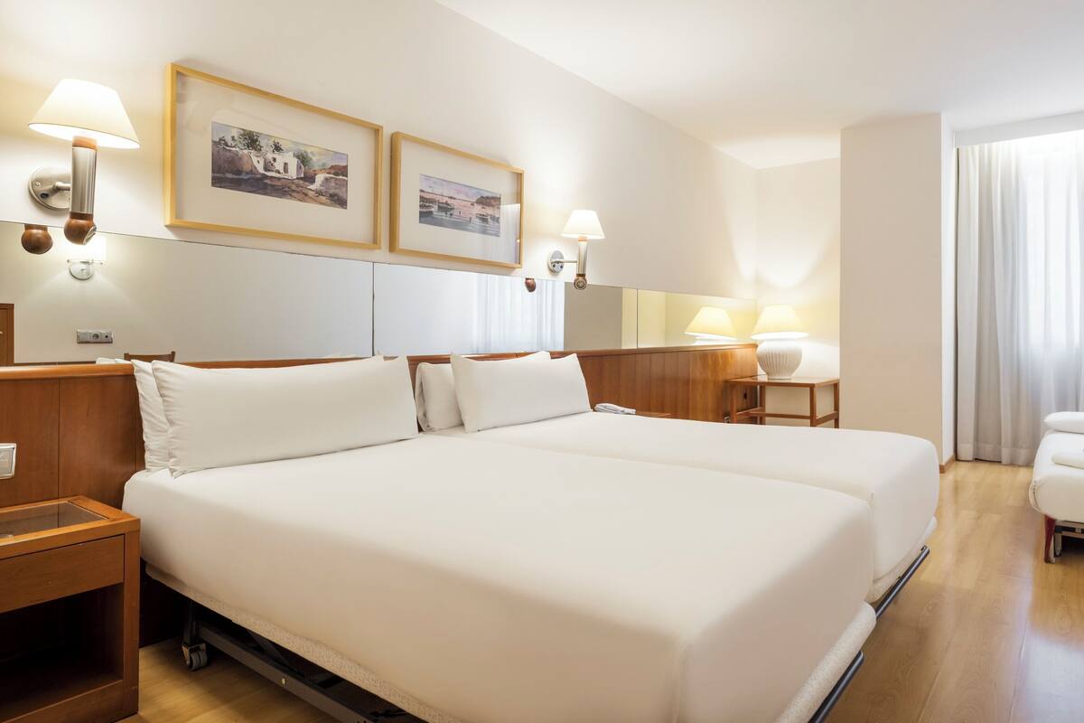A hotel room with a large bed, two bedside tables, a desk, a chair, and a window with curtains.