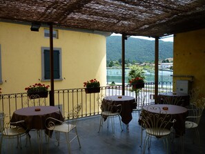 An outdoor patio with yellow walls, metal chairs, round tables, and flower planters.