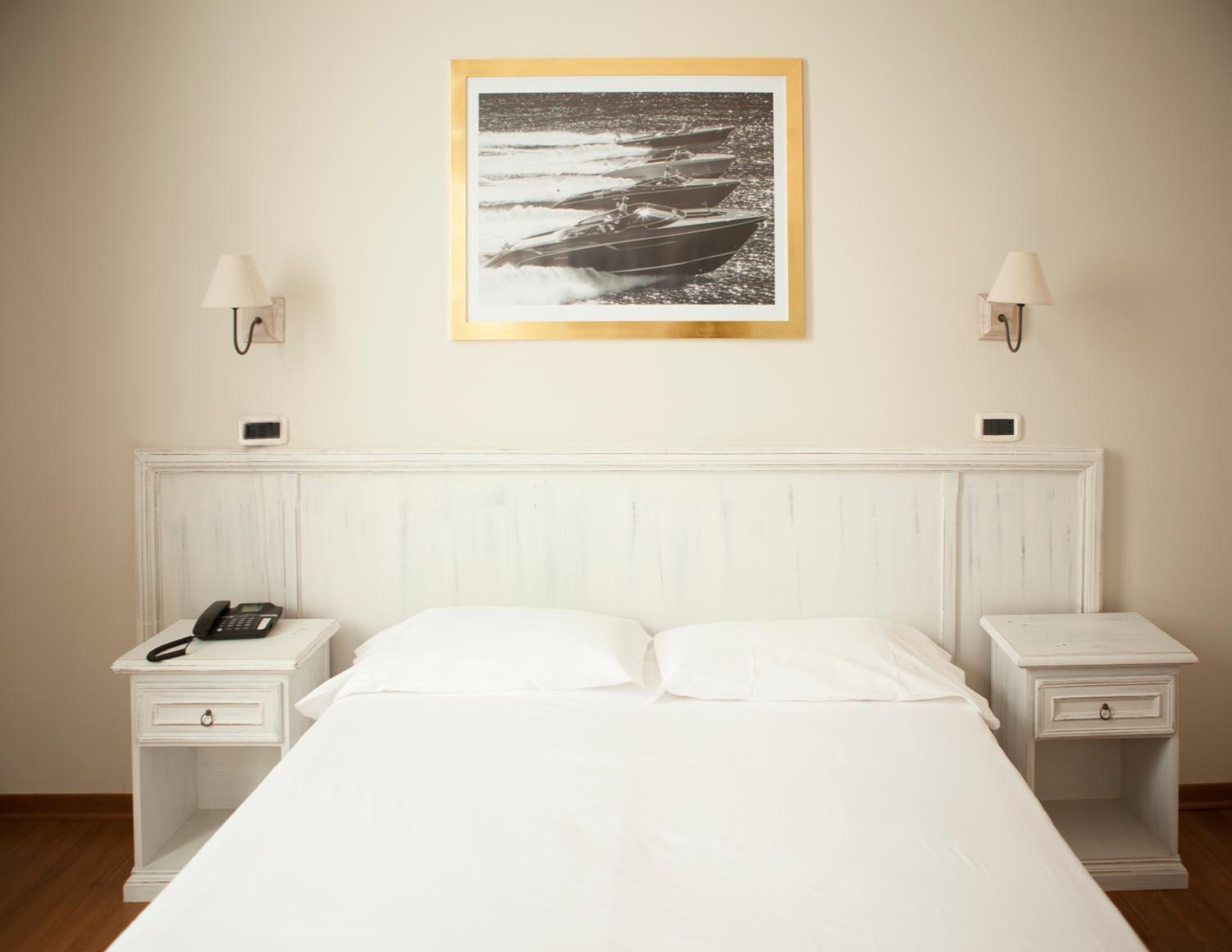 Een keurig opgemaakt hotelkamer met een bed, twee nachtkastjes, een wandlamp en een lijst met een foto boven het bed.