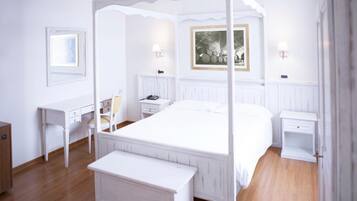 A four-poster bed with a white canopy, a desk with a chair, a bedside table with a lamp, and a framed picture on the wall.