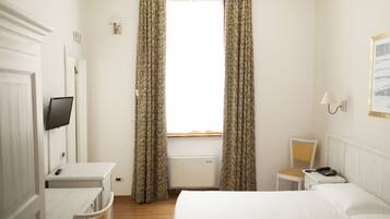 Una camera d'albergo con un letto, una scrivania, una sedia, un comodino con un telefono e una TV a muro.