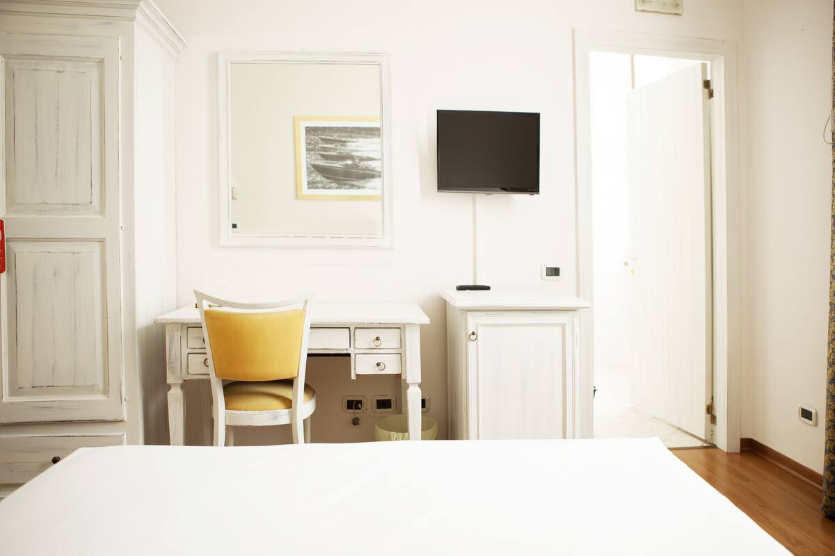 A room with a bed, a desk with a chair, a television, and a door.