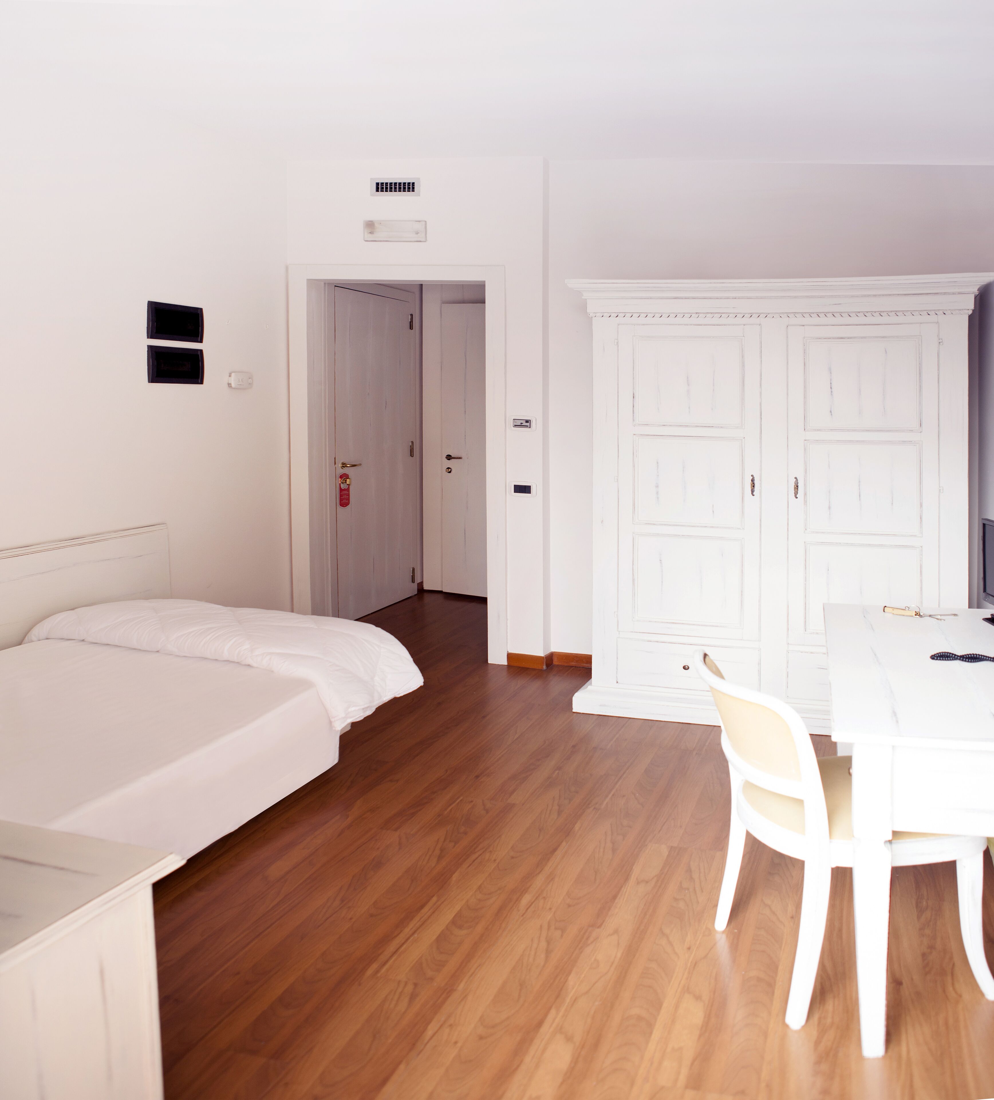 A room with a bed, a desk, and a chair. There is a door leading to another room.