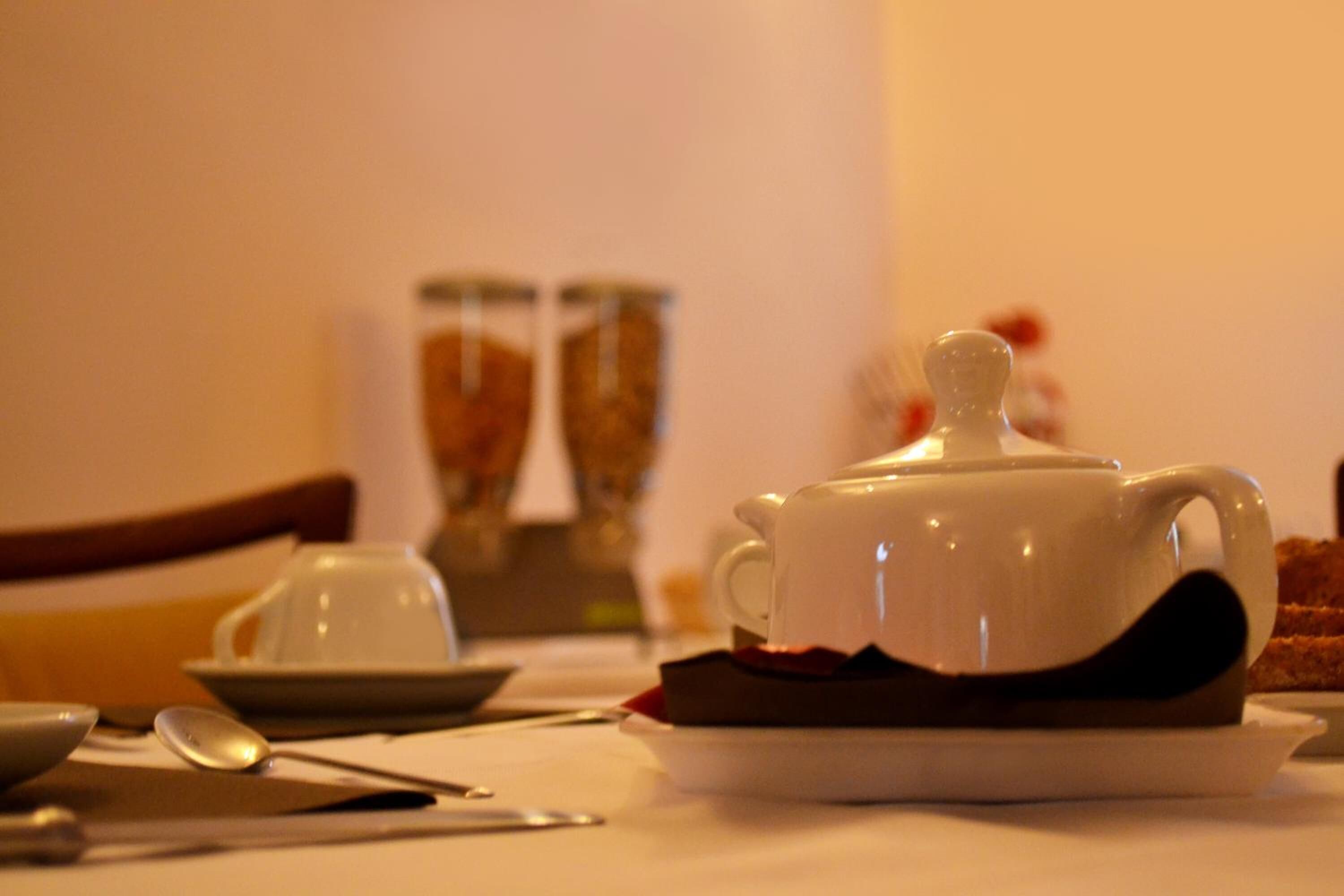 A dining table with a white teapot, a cup, and a plate with food.