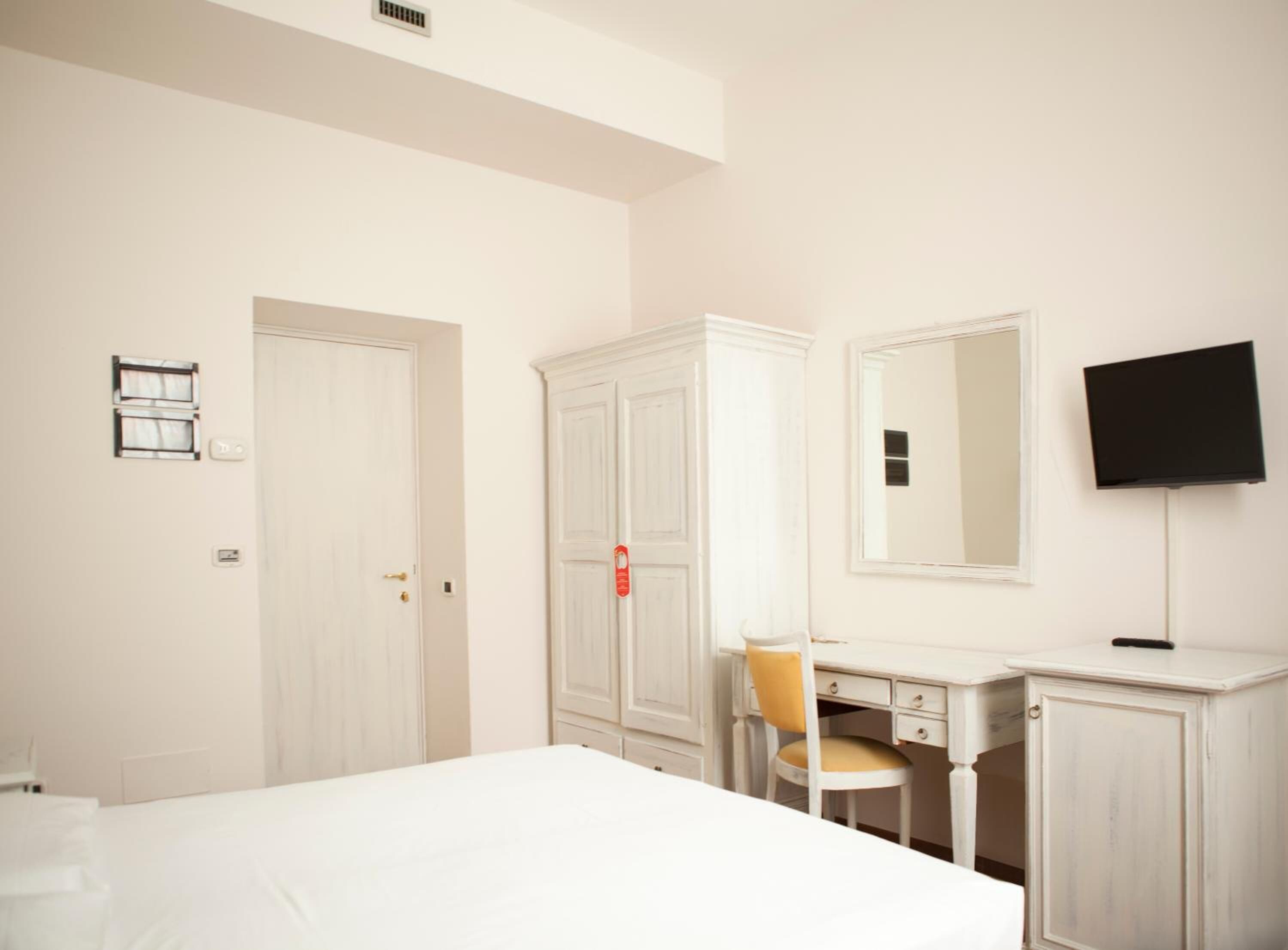 Een hotelkamer met een bed, een bureau met stoel, een kledingkast, een televisie en een spiegel.