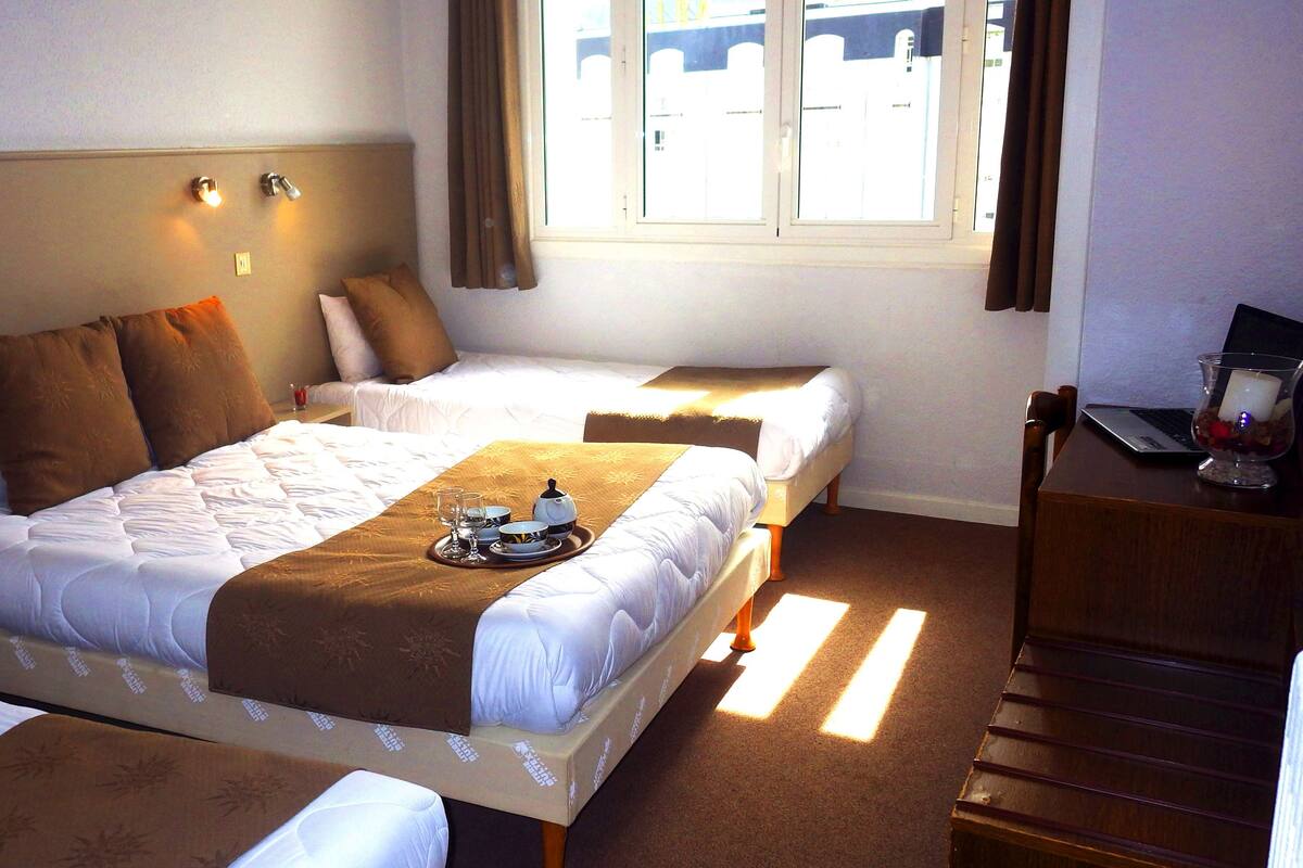 A hotel room with two single beds, a desk with a laptop, and a window with curtains.