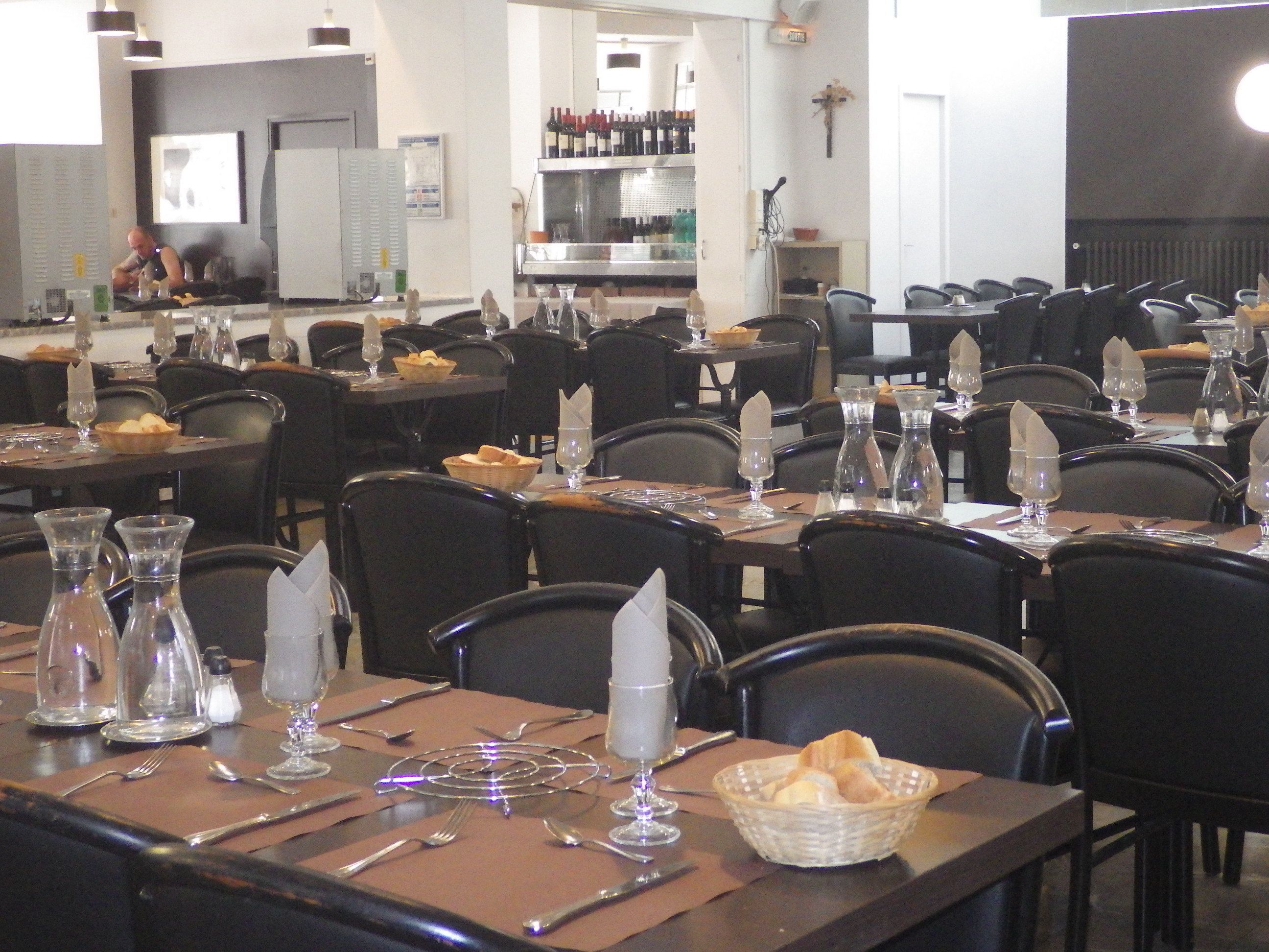 Een restaurant met meerdere gedekte tafels, elk met bestek, glazen en broodmanden.