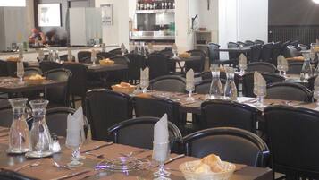 A restaurant with multiple tables set for dining, each with cutlery, glasses, and bread baskets.