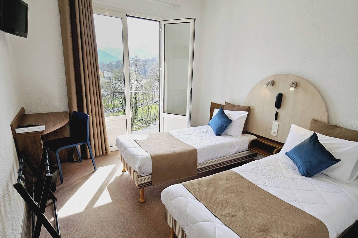 A hotel room with two beds, a desk, a chair, and a TV.