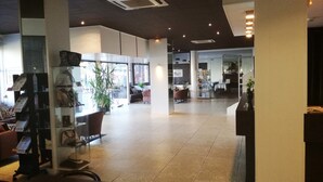 A spacious lobby with a reception desk, seating area, and a glass partition separating the lobby from the dining area.