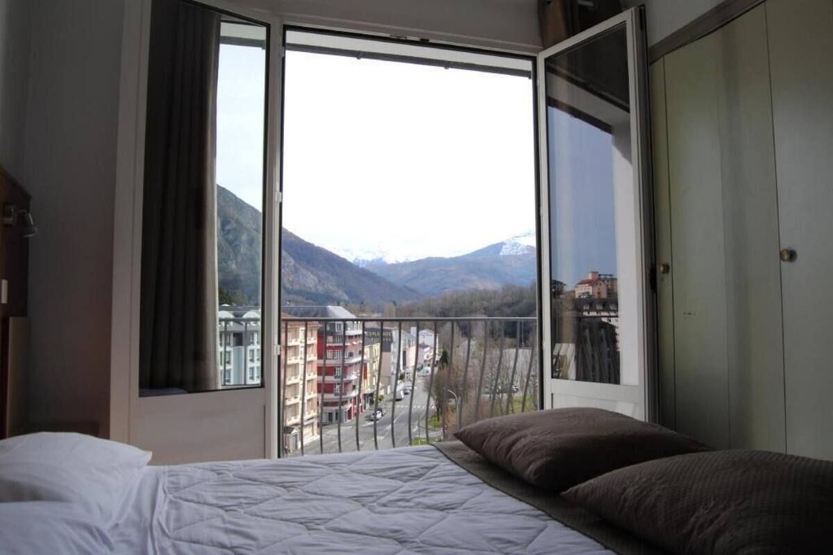 A bedroom with a large window, a bed, and a view of a mountain and buildings.