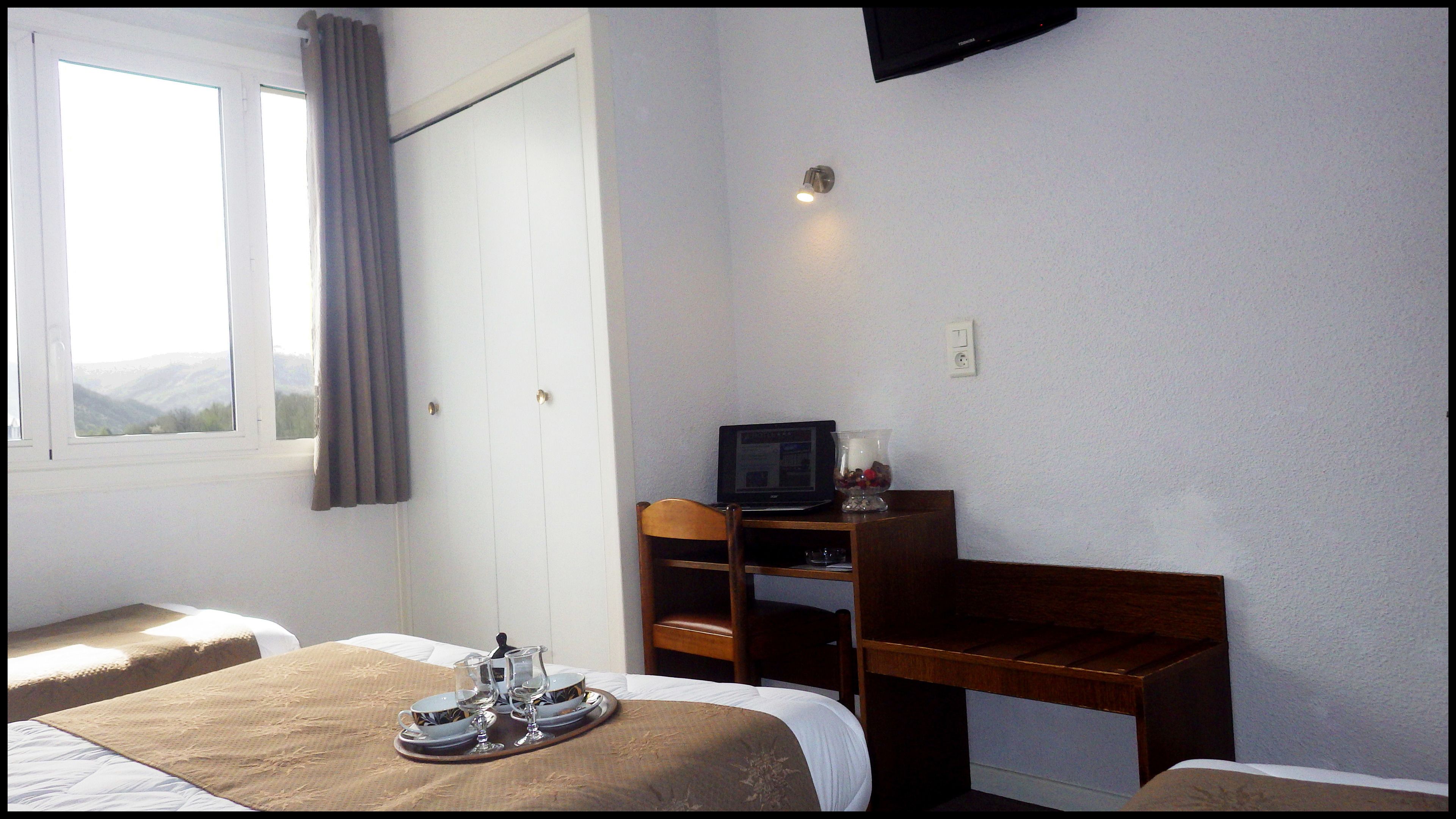 Ein Hotelzimmer mit zwei Betten, einem Schreibtisch mit Fernseher und einem Fenster mit Bergblick.