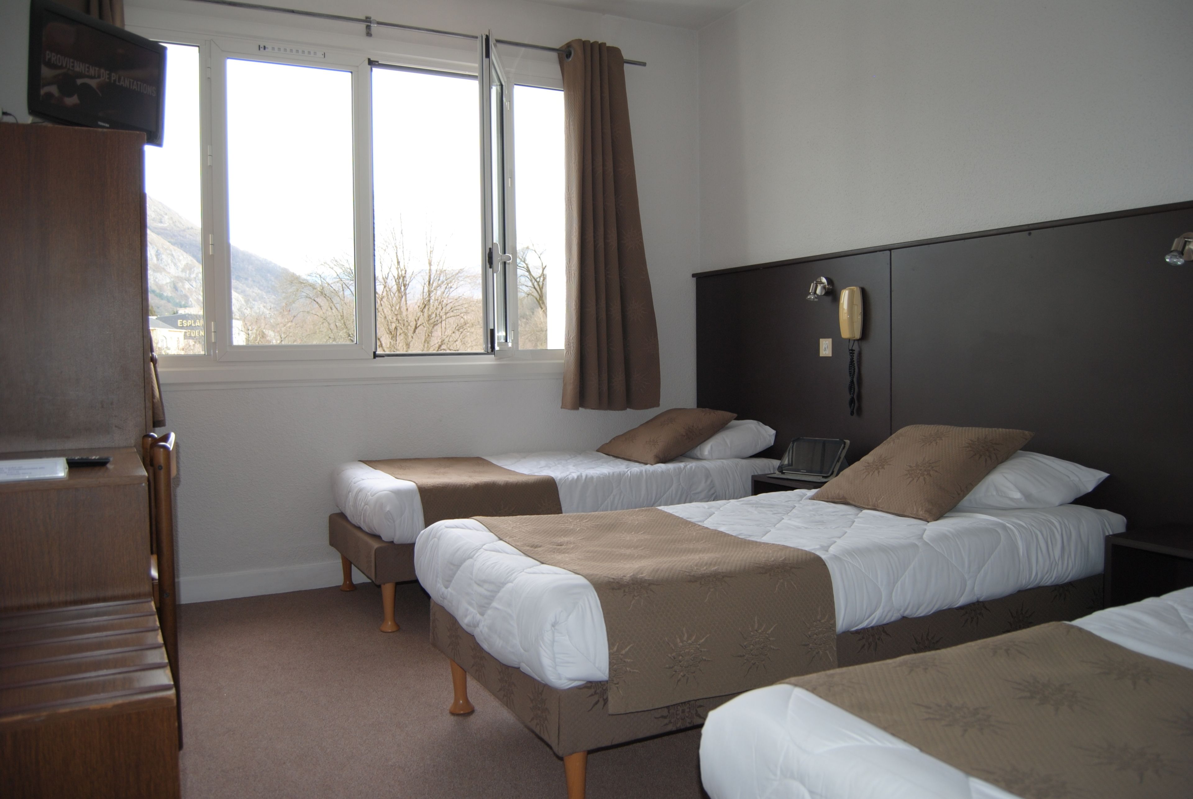 Une chambre d’hôtel avec deux lits simples, un bureau en bois et une grande fenêtre avec des rideaux.