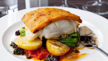 Un plato de comida con un filete de pescado, papas, judías verdes y salsa de tomate.