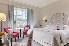A hotel room with a large bed, a sitting area with a table and chairs, a view of the sea, and a patterned headboard. - Actons Hotel (Kinsale)